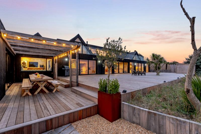 A holiday let on the East Sussex coast at dusk, its decking lit with string lights and the outdoor dining table laid